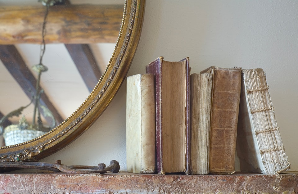 Degli antichi libri poggiati sulla mensola di un camino accanto a uno specchio dalla cornice vintage