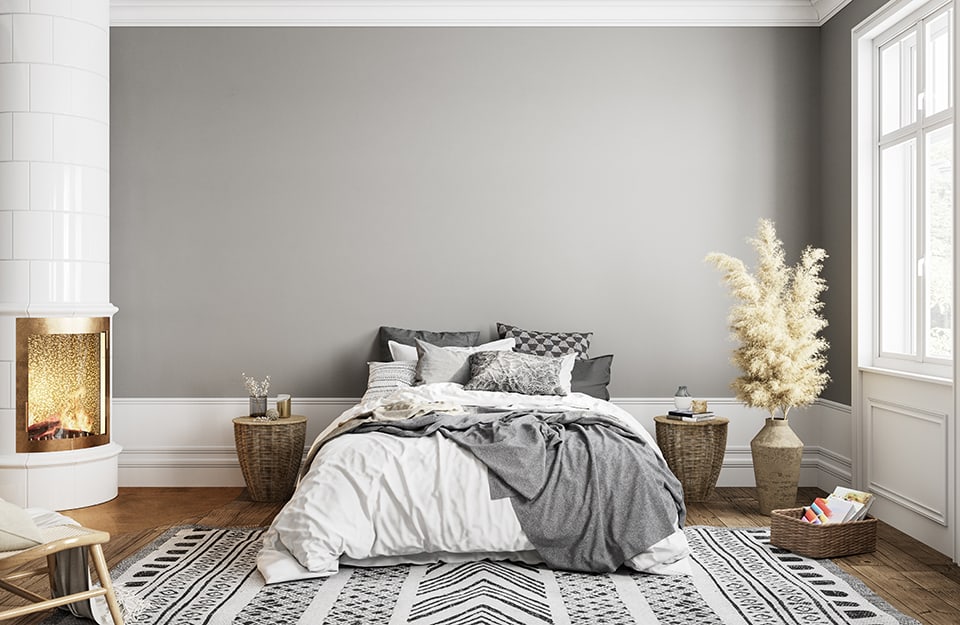 Luminosa camera da letto sui toni del grigio: grigia la parete e il tappeto sotto al letto. Grigi anche i cuscini e la coperta