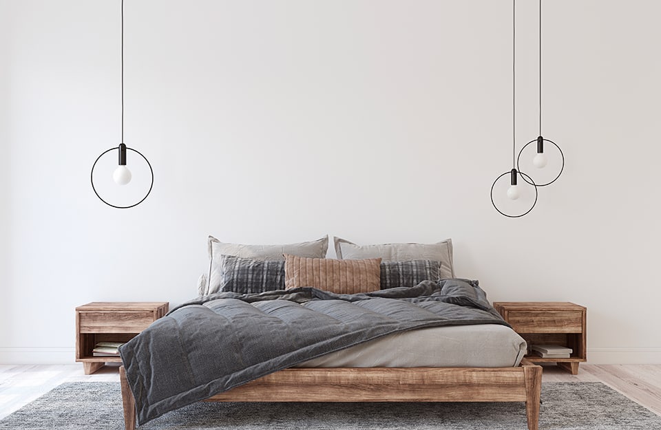 Camera da letto in stile minimale con tre lampadari a cerchio, mobili in legno e biancheria grigia