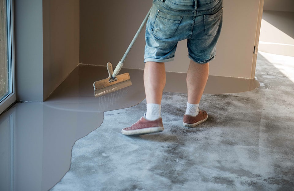 Un uomo in pantaloncini corti sta ricoprendo un pavimento con la resina in un'abitazione