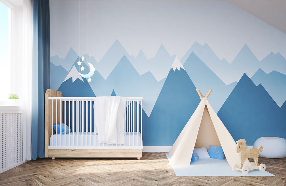 Una cameretta per neonati con pareti decorate con immagini di montagne. C'è anche una piccola tepee per giocare