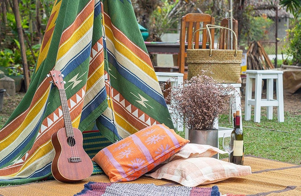 Un angolo decisamente Bohémien, in giardino, con una stuoia, tenda con pattern etnici, cuscini orientaleggianti, chitarra e bottiglia di vino