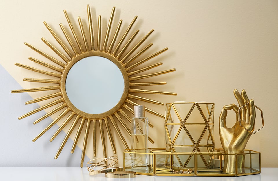 Una composizione di nature morte dorate, tra oggetti, soprammobili e uno specchio con cornice a raggiera