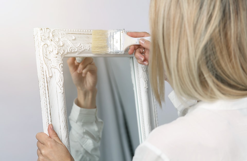 Donna dipinge uno specchio bianco in stile shabby chic