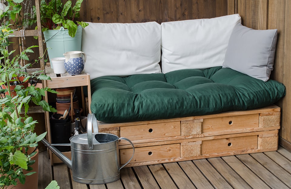 Una piccola terrazza piena di piante e con all'angolo un divano in pallet coi cassetti