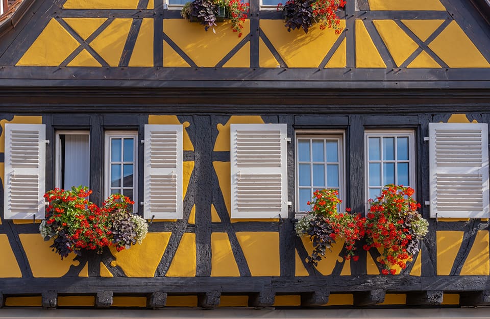 Primo piano su una peculiare casa con travi esterne a vista e colori accesi di Colmar, in Francia. La casa è di colore giallo