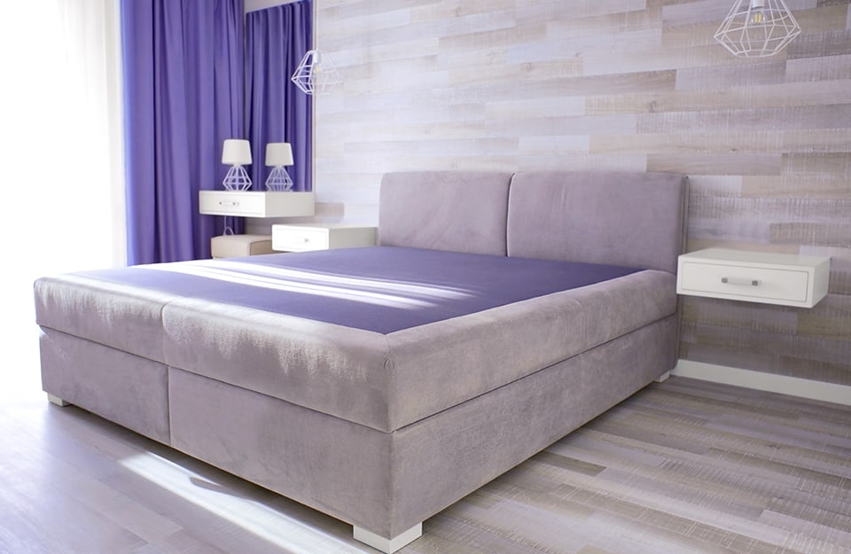 Camera da letto moderna e minimale sui toni del grigio, con tenda e coperta di color Very Peri, il colore dell'anno 2022 secondo Pantone