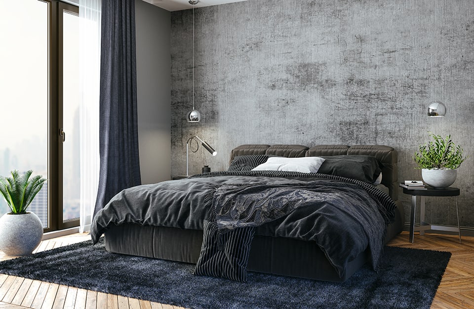 Camera da letto con muro in cemento grezzo e pavimento in legno. C'è un grande finestrone. La biancheria è nera, così come il tappeto sotto il letto