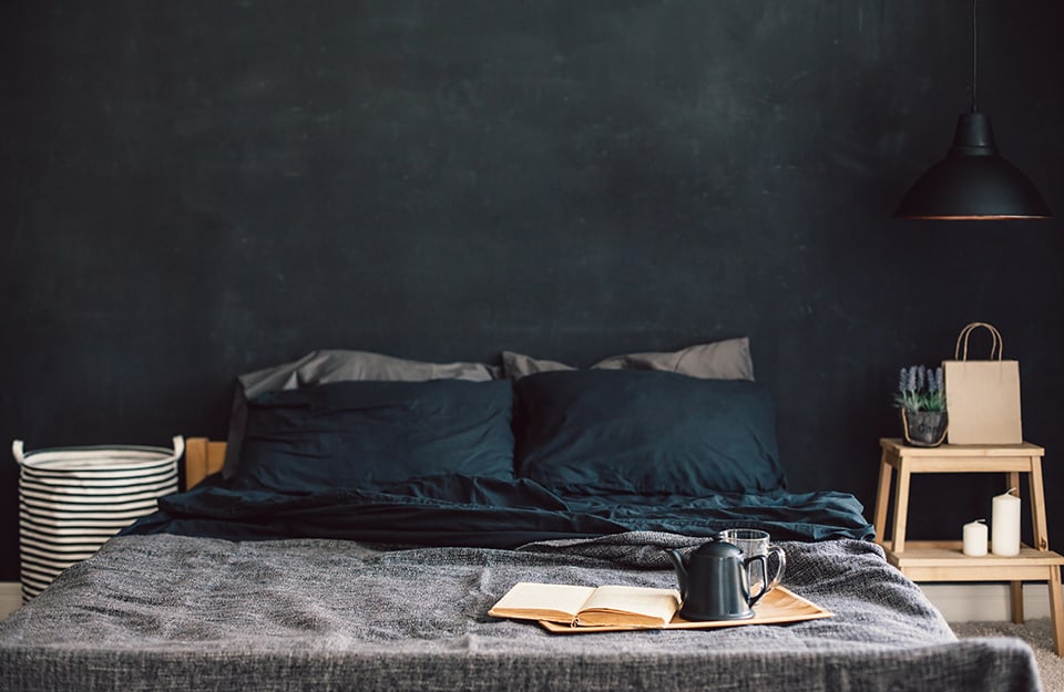 Camera da letto con pareti nere, cuscini neri e copriletto grigio. Sopra alla coperta c'è un vassoio con la colazione
