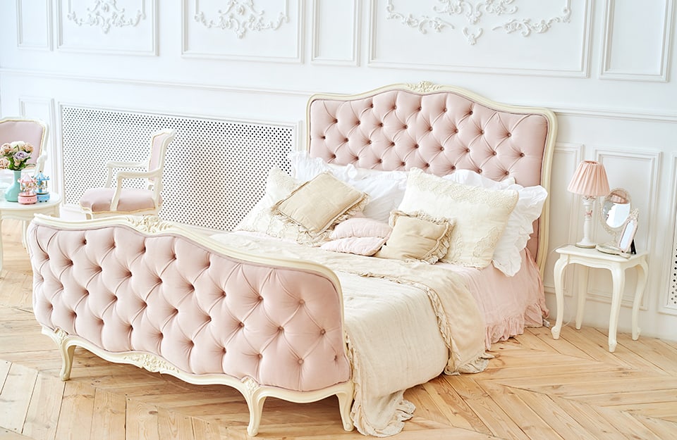 Camera da letto in stile vintage romantico. Le pareti sono bianche e decorate e il letto ha la testiera rosa con le impunture