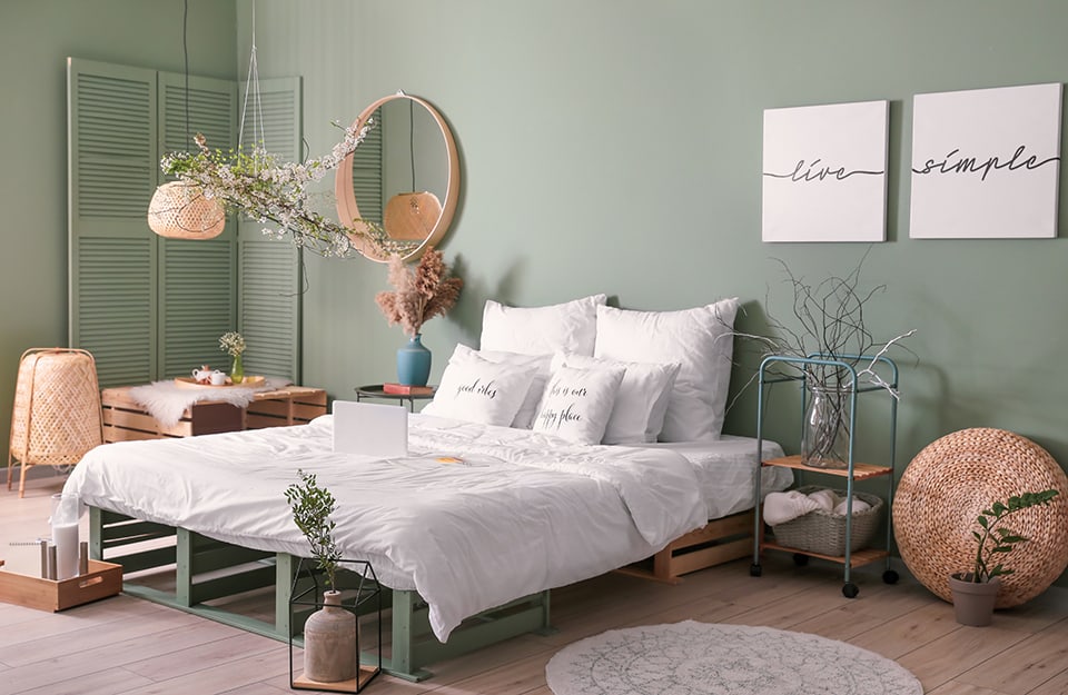 Camera da letto con pareti verdi e diversi accessori in legno, metallo e rattan