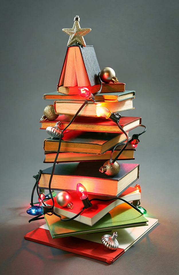 Albero di Natale creato mettendo in equilibrio libri, luci e palline
