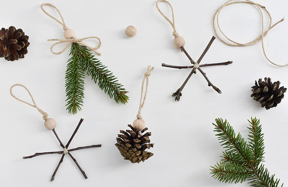 Delle decorazioni natalizie low-cost create con spago, sfere di legno che reggono pigne e rametti