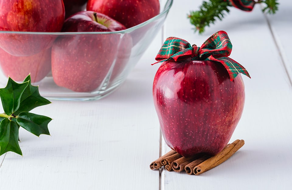 Una mela decorata con fiocchetto e stecche di cannella da utilizzare come segnaposto per la tavola di Natale