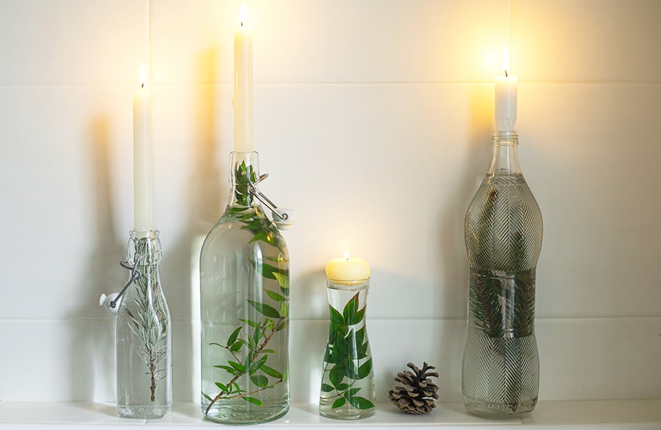 Quattro candele accese fissate su altrettante bottiglie di vetro riempite d'acque e di ramoscelli di piante