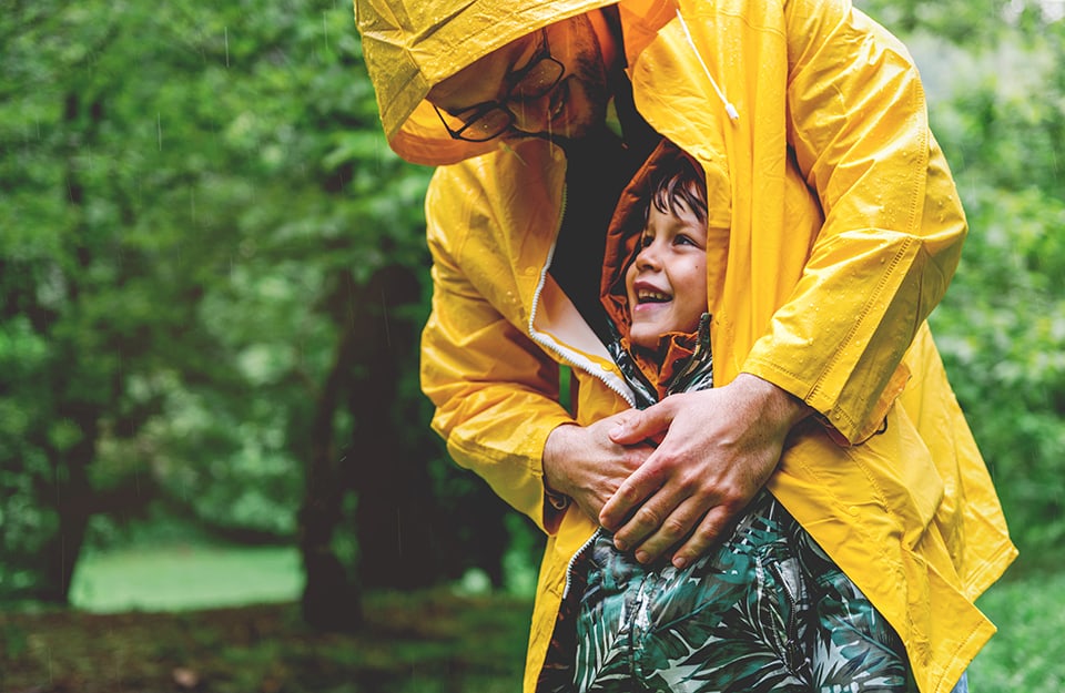 Padre e figlio all'aria aperta sotto la pioggia, felici e avvolti in un impermeabile giallo