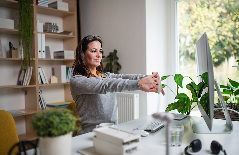 Donna che si sgranchisce le mani mentre lavora al computer nel suo accogliente e luminoso ufficio casalingo pieno di piante in vaso