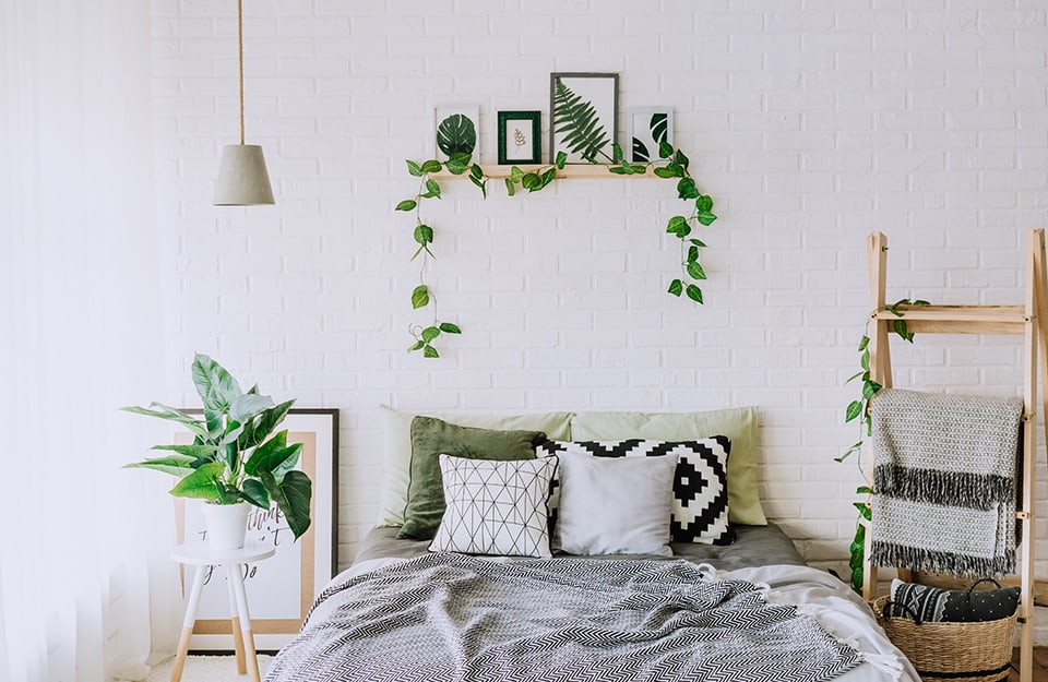 Luminosa stanza da bianco sui toni del bianco e del legno, con molte piante, anche su una mensola sopra al letto