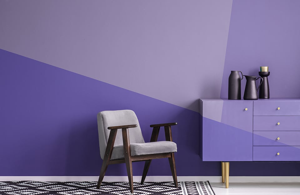 L'angolo di un salotto tutto sui toni del viola, in stile color block, con contrasti cromatici sulla parete e sulla consolle