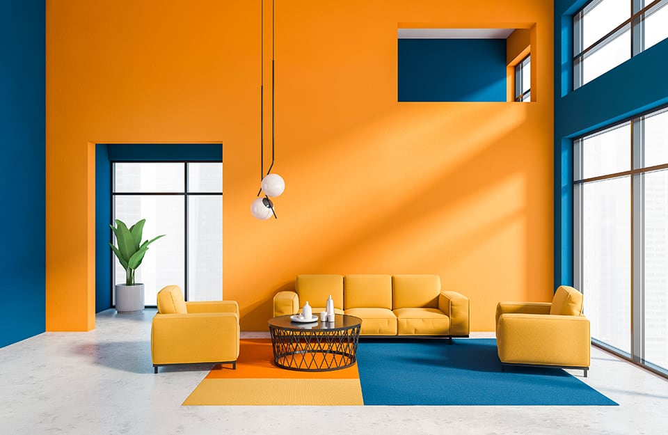 Salotto moderno in un ambiente dal volume molto ampio, decorato a contrasto con pareti blu e arancio, colori applicati anche al tappeto e alle sedute