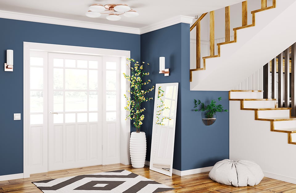 Ingresso di una casa, con scale che portano al piano superiore. Alcune pareti sono dipinte in blu, a contrasto col bianco