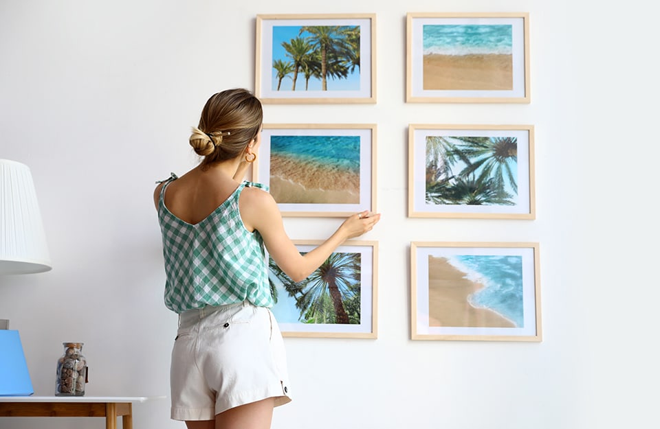 Una donna in shorts appende alla parete una composizioni di grandi foto delle vacanze in luoghi esotici