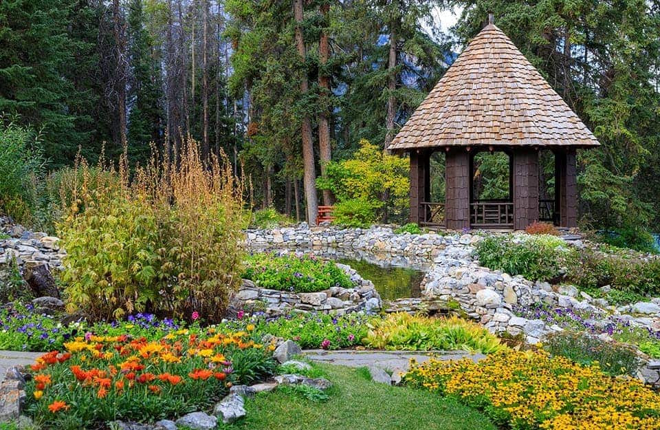 Un giardino roccioso lussureggiante con un gazebo con tetto conico. Sullo sfondo c'è un bosco