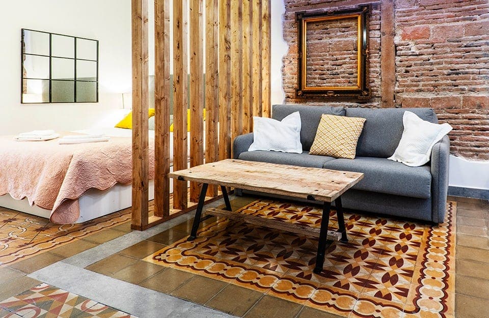 Ambiente con salotto e camera da letto divise da separé in legno e pavimenti in maiolica