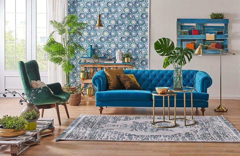 Un salotto in stile eclettico, con arredi dai molti stili, carta da parati a pattern azzurri e molte piante