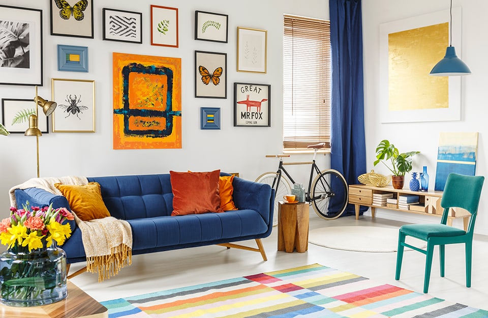 Coloratissimo salotto in stile eclettico con tappeto a motivi geometrici, divano blu e molte stampe appese alla parete