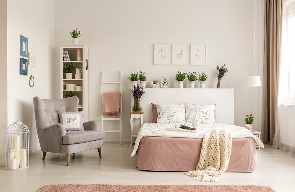 Una camera da letto moderna che strizza l'occhio allo stile provenzale, con molto bianco e colori pastello e piante di lavande sparse per la stanza
