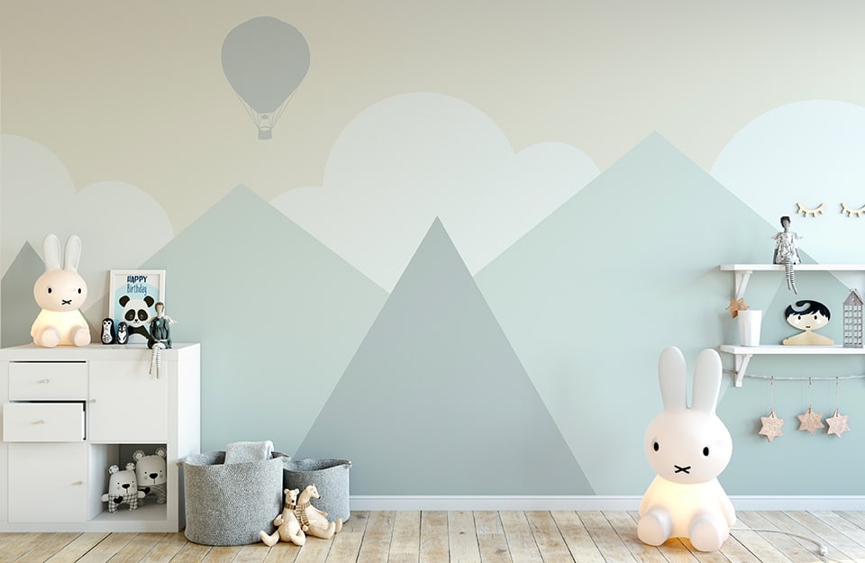Cameretta dei bambini in stile scandinavo con pareti decorate con l'immagine color pastello di un paesaggio stilizzato con montagne, nuvole e una mongolfiera
