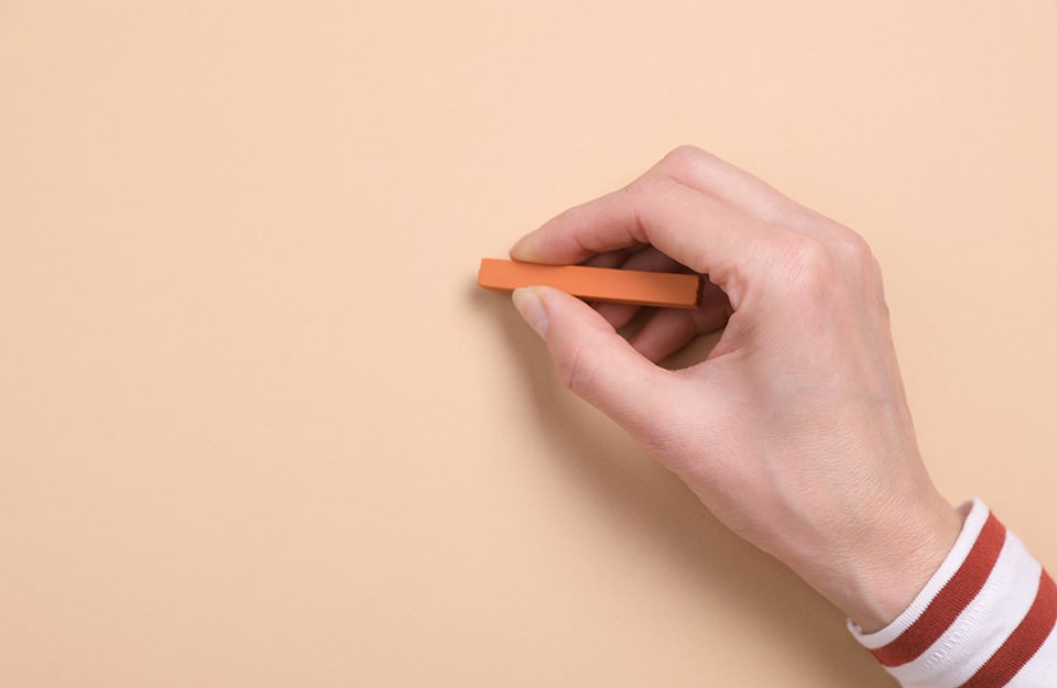 Una mano disegna con un pastello morbido arancione su una superficie color rosa salmone