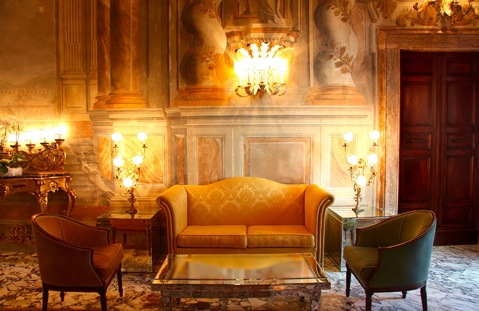 Grande sala in stile barocco antico, con sofà, poltrone, dettagli in marmo, pareti con trompe-l'oeil, pavimento in marmo e arredi barocchi