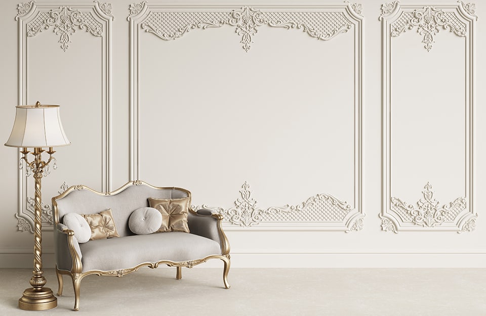 Stanza con pareti decorate sul beige molto chiaro, con lampada a stelo dorata in stile barocco e un divano tappezzato con tessuto grigio e struttura in legno dorato