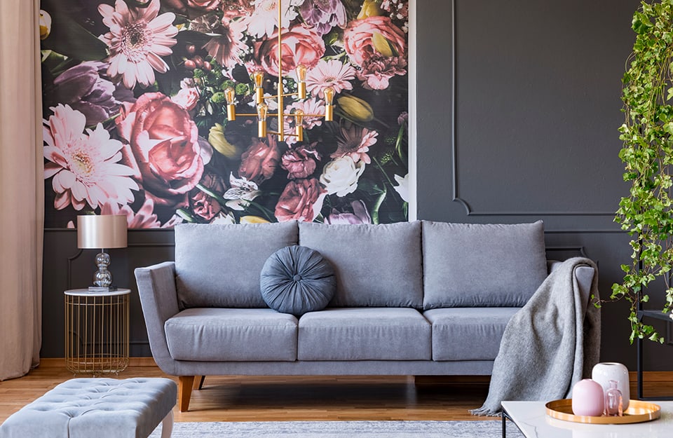 Salotto in stile scandinavo con sofà grigio e parete di fondo grigio scuro con cornici vintage e una grande stampa floreale applicata al muro