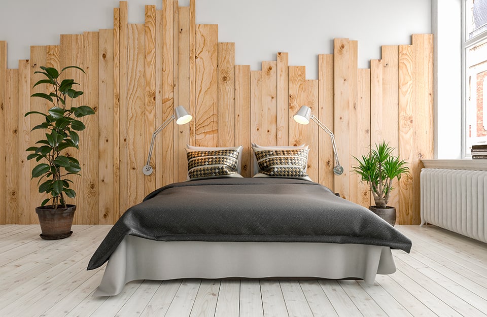 Camera da letto luminosa con parete dietro al letto decorata con una composizione di assi di legno installate in verticale e dalle lunghezze irregolari