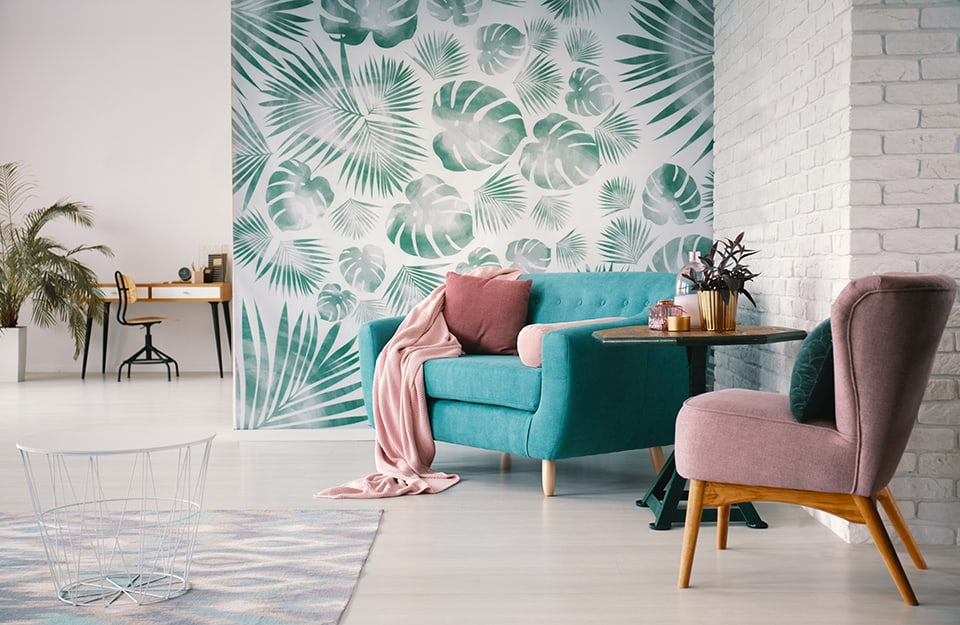 Salotto vintage con poltrone diverse e colorate, separato da un altro ambiente attraverso una parete con carta da parati decorata con motivo botanico bianco e verde