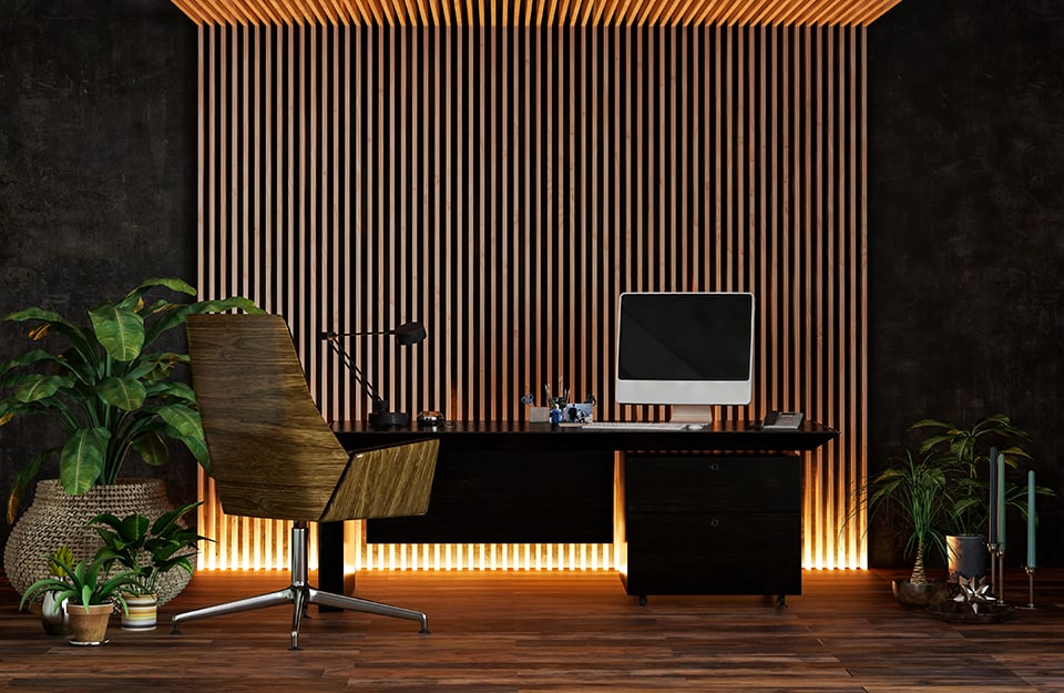 Angolo studio con scrivania e sedia, davanti a una porzione di parete decorata con sottili elementi in legno evidenziati e illuminati da luci dal basso verso l'alto
