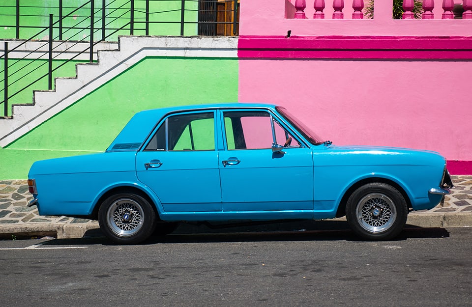 Una auto blu d'epoca parcheggiata tra due edifici colorati (una verde e uno rosa) del quartiere di Bo-Kaap a Città del Capo