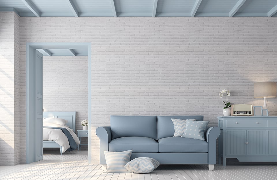 Casa moderna in stile essenziale sui toni del bianco e dell'azzurro. Le pareti sono bianche, il soffitto azzurro, come il sofà e i mobili e si intravede da una porta la camera da letto