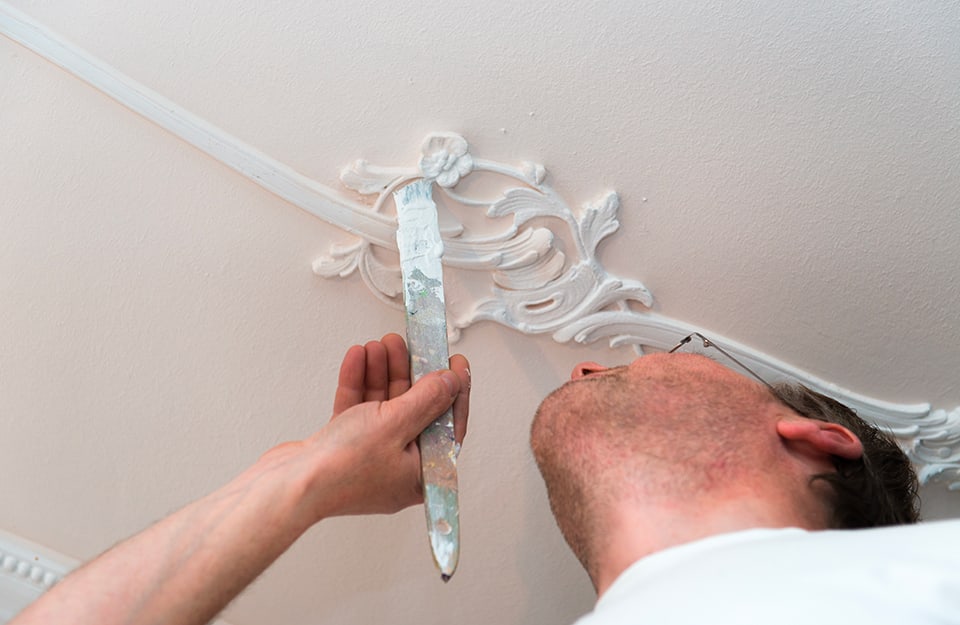 Un uomo sta verniciando una decorazione a stucco sul soffitto