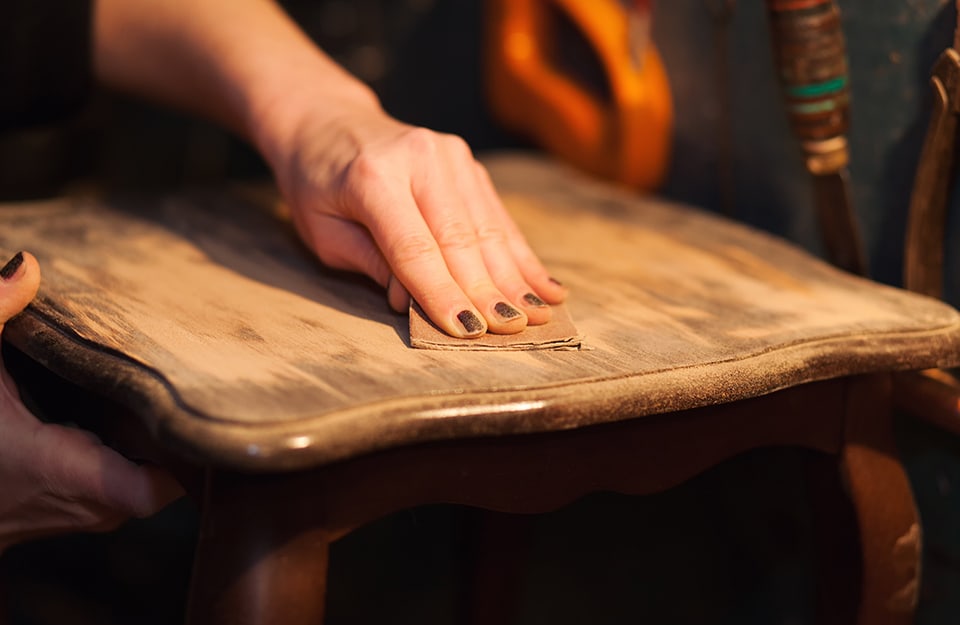 Una mano femminile sta carteggiando un tavolino vintage da restaurare