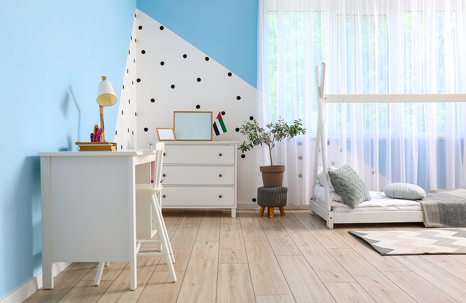 Bedroom with blue walls and white geometric area with black polka dots. Parquet floor, white wooden bed with curtain structure, white chest of drawers and white desk