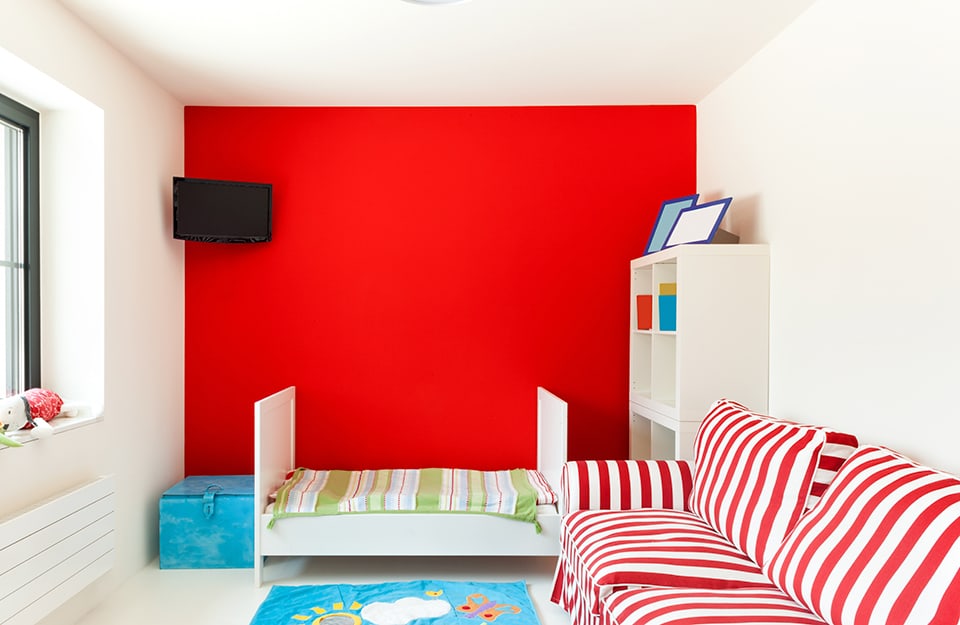 Small bedroom with white walls, ceiling and floor, red back wall, white bed and red-and-white striped sofa; 