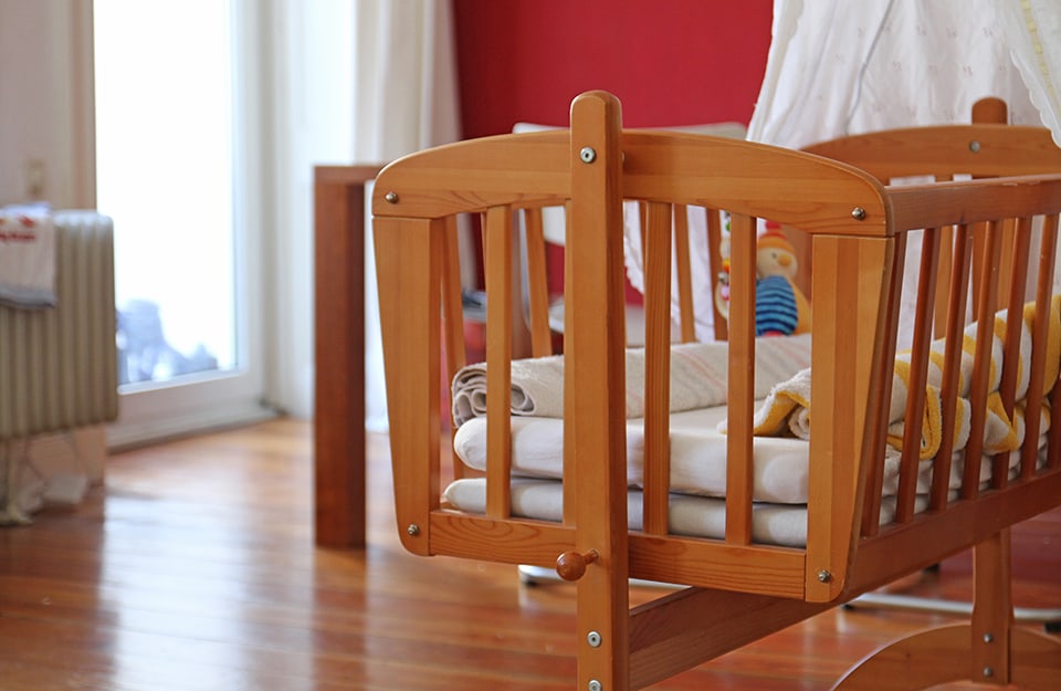 Wooden baby cot in modern style in bedroom with parquet floor and red-painted wall
