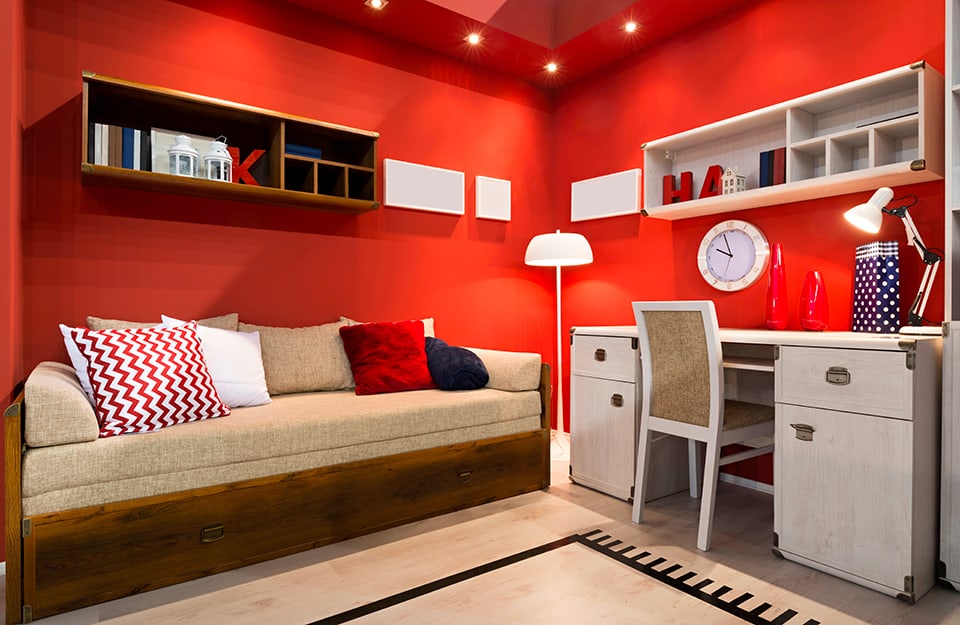 Camera per ragazzi con pareti e soffitto rosso, faretti a soffitto, divano modernista, tappeto, scrivania bianca, lampada a stelo e scaffali a parete