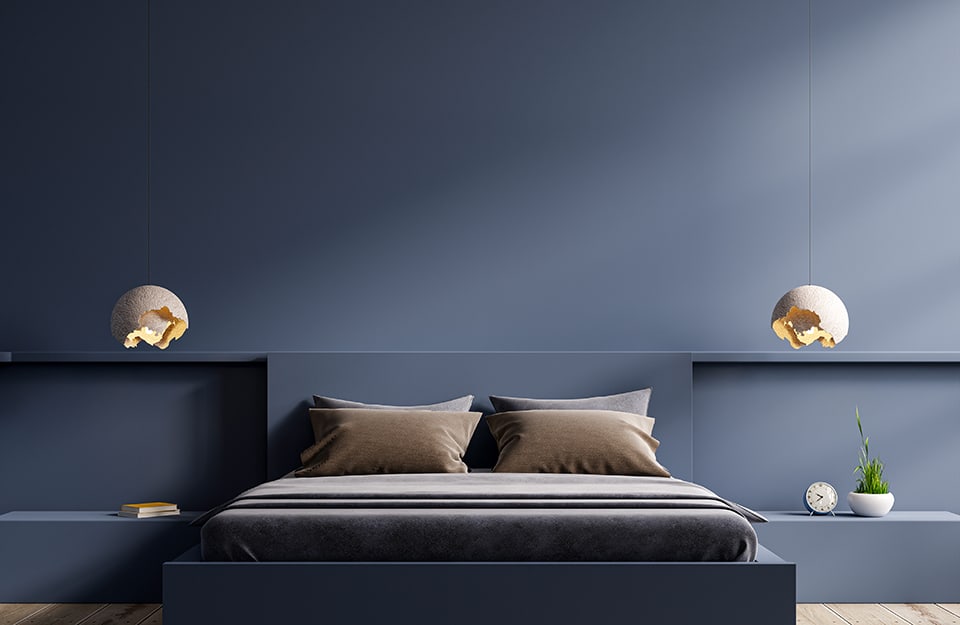 Ultra-minimal bedroom, with bed frame, bedside tables and walls in the same colour (blue). Two disjointed sphere-shaped chandeliers descend from above;