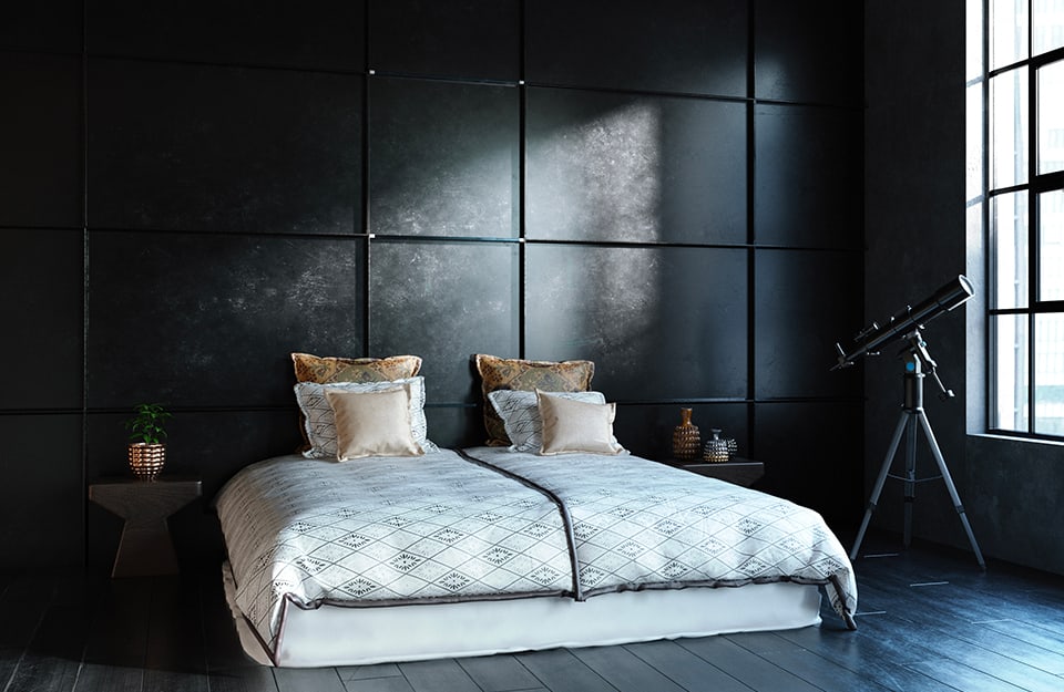 Spacious bedroom in industrial open space all in black (black is the squared metal wall and black is the parquet floor). The bed is white, with twin duvets. On the two bedside tables are jars and next to the bed is a black telescope pointing to the sky outside the large window;