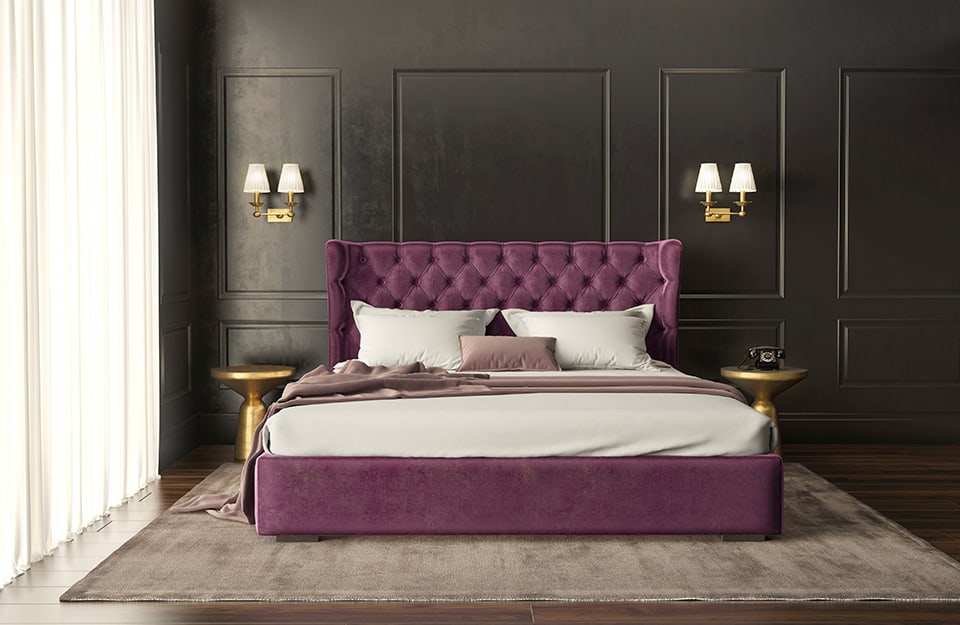 Large bedroom with black framed walls, double gold metal wall lamps on each side of the bed, purple quilted headboard, metallic bedside tables, large carpet under the bed, parquet floor, and white curtain covering the window;